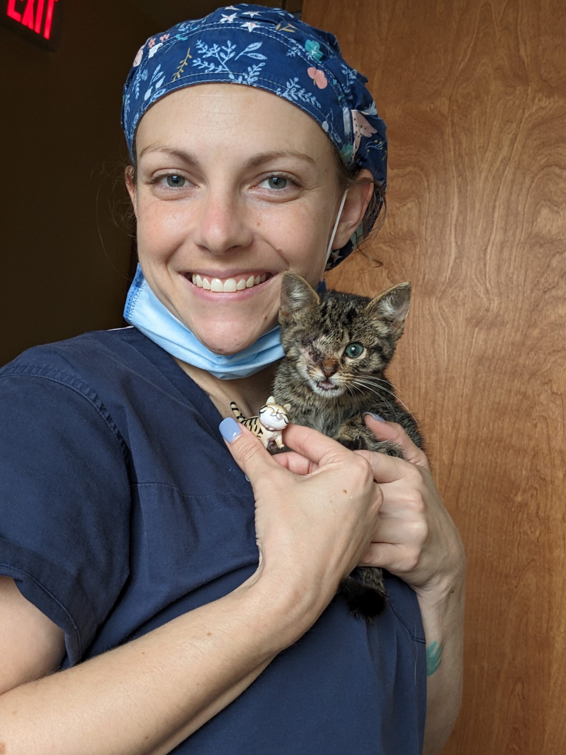 a person wearing scrubs and a blue head wrap holding a kitten